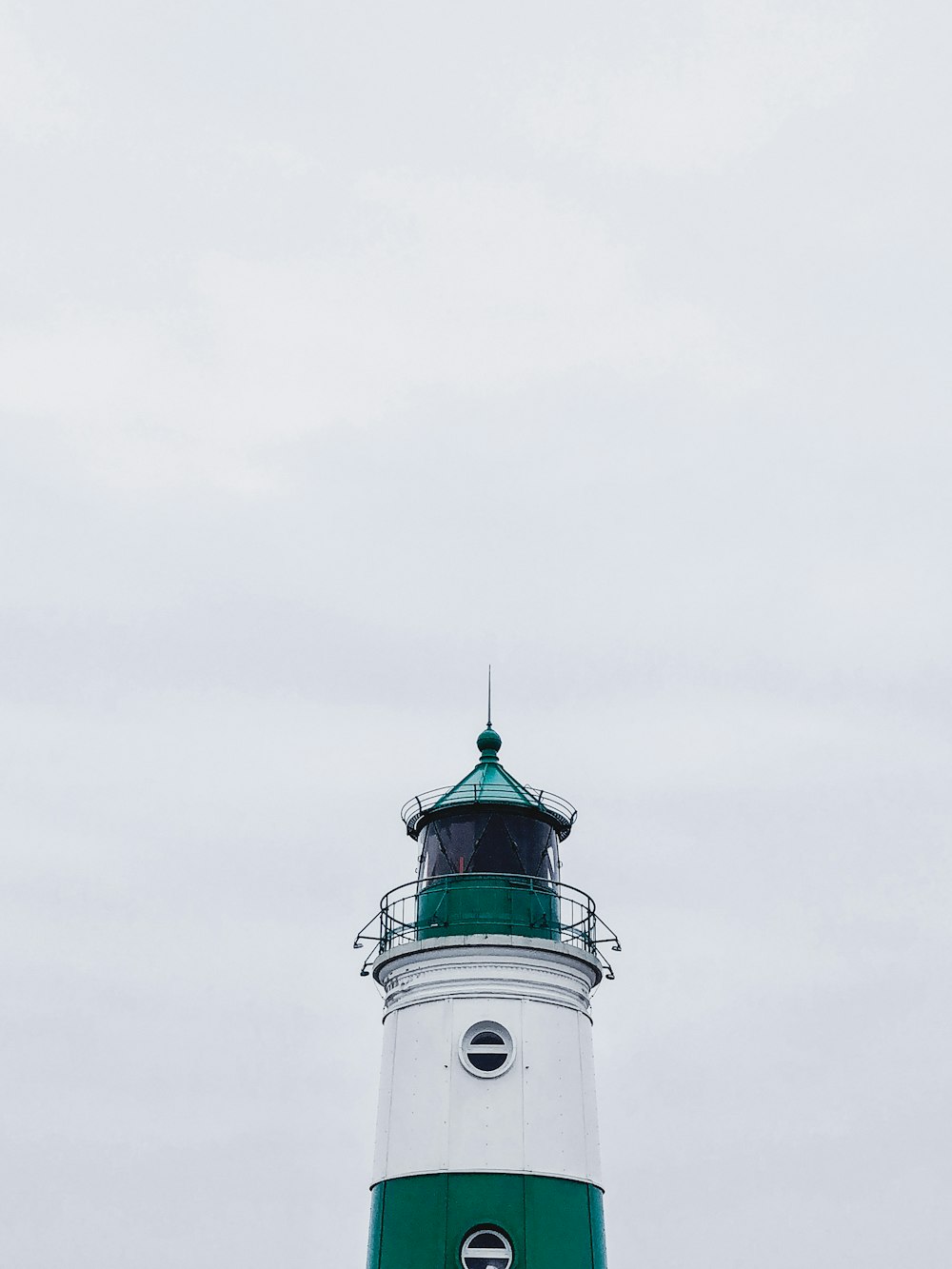 昼間の白い空の下に白と緑の灯台