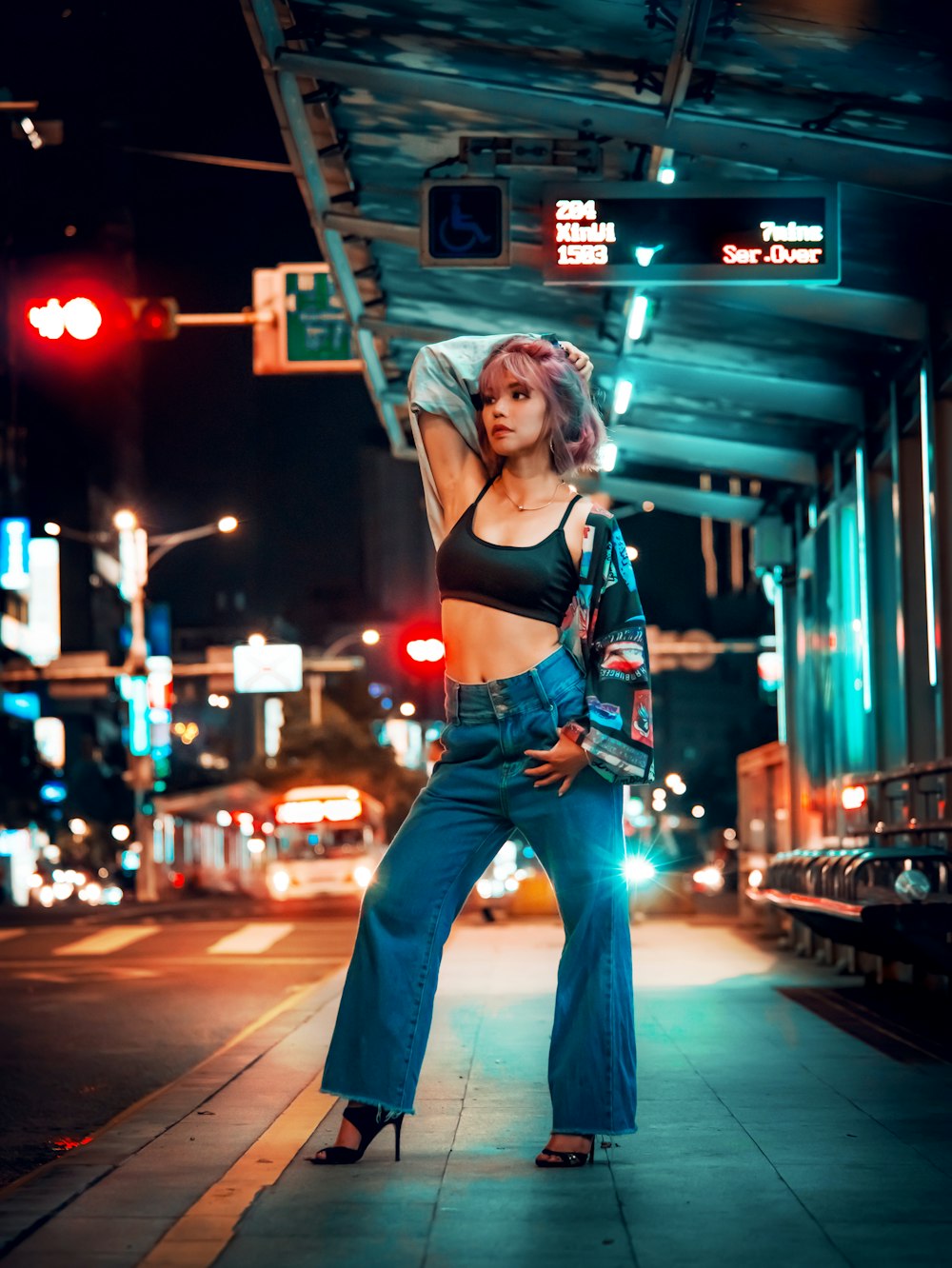 woman in red sports bra and blue denim jeans standing on sidewalk during night time