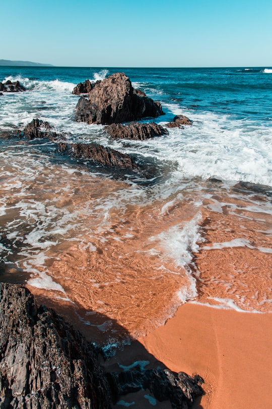 brown rocky shore with ocean waves during daytime in Plettenberg Bay South Africa