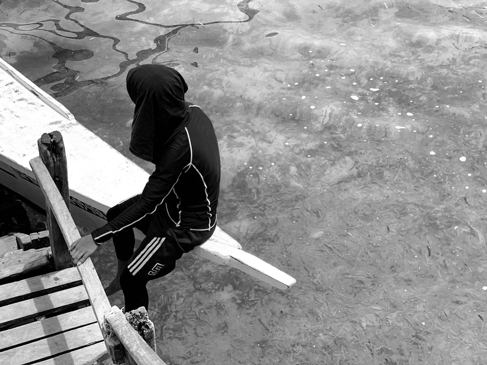 Hombre con sudadera con capucha negra y pantalones negros caminando sobre pavimento de concreto