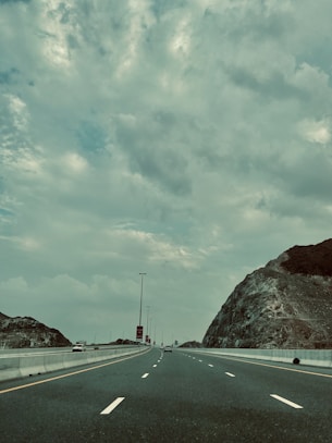 Monochrome image of a long stretch of highway disappearing into the horizon under cloudy skies.