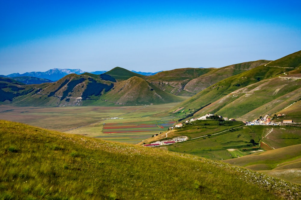 green grass field near mountain under blue sky during daytime