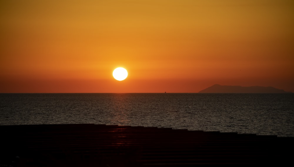 the sun is setting over the ocean with a small island in the distance