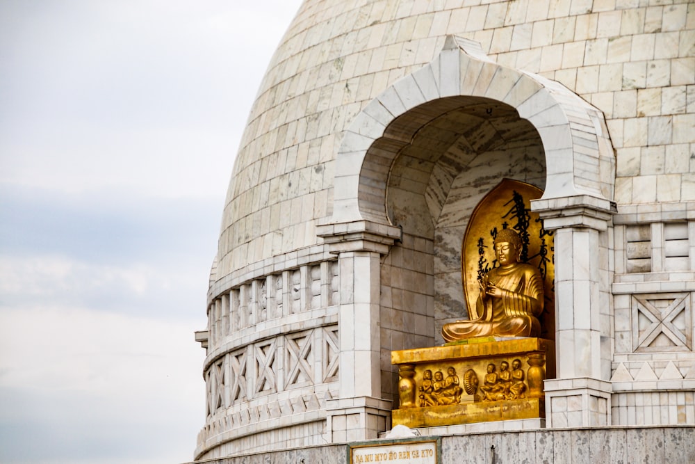 Goldene Buddha-Statue in der Nähe eines weißen Betongebäudes tagsüber