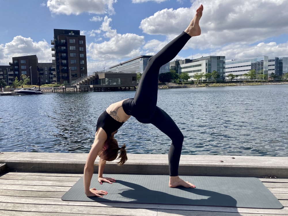 woman in black tank top and black leggings doing yoga near body of water during daytime