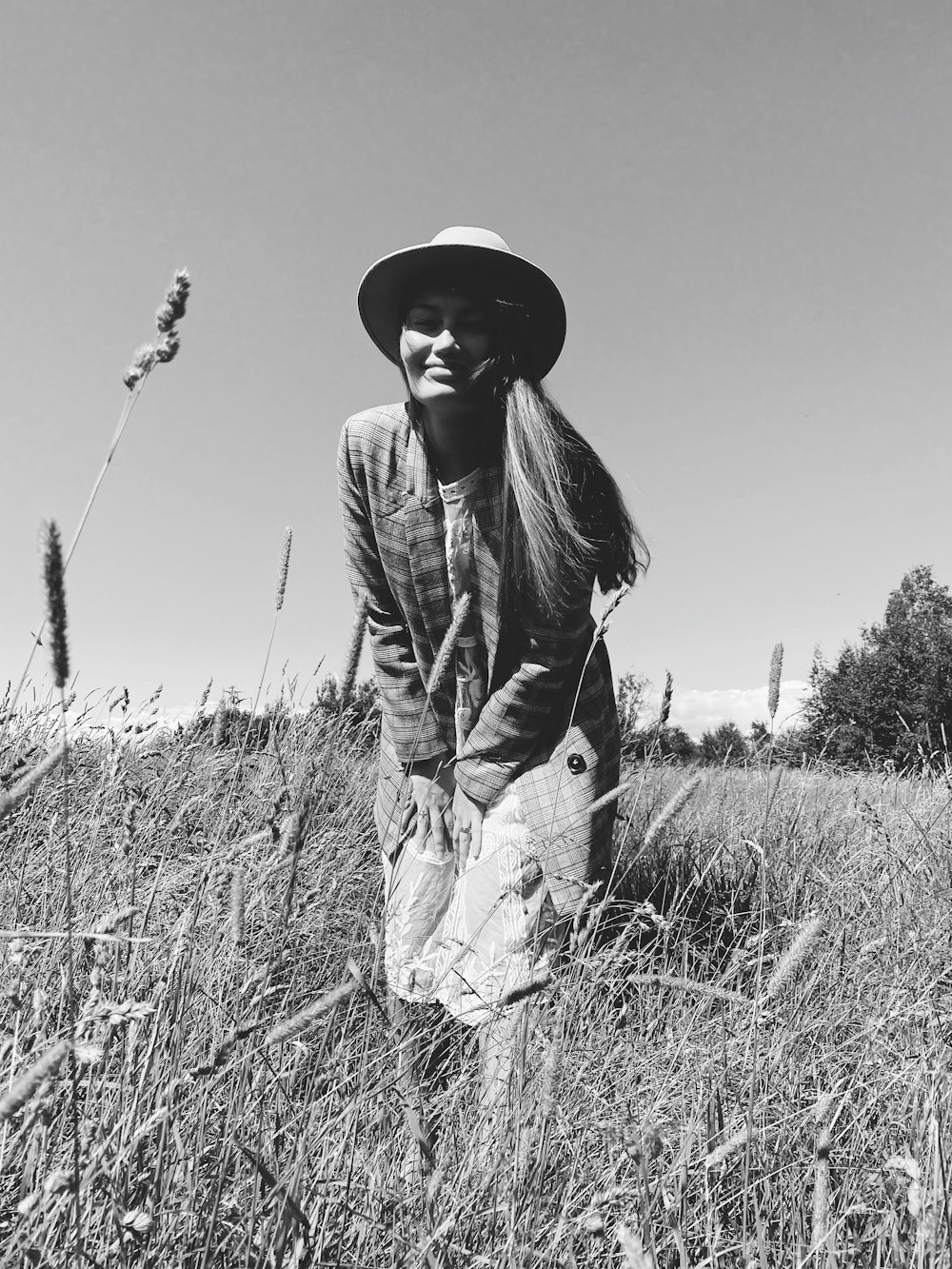 grayscale photo of woman in black leather jacket and hat standing on grass field