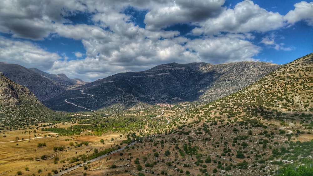 green grass field and mountains under white clouds and blue sky during daytime