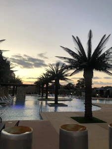 A serene view of the hotel's pool area with the sea and Kızkalesi castle visible in the background at sunset.
