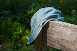 A stylish cap in olive green perched on a rustic fence post against a clear sky.