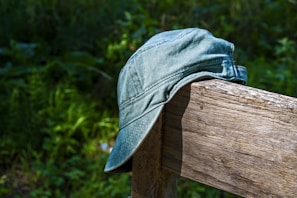 A stylish cap in olive green perched on a rustic fence post against a clear sky.