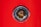 A close-up view of a metal bolt or screw embedded in a vibrant red surface. The metal is slightly rusted and set within a shiny, silver-colored circular frame.