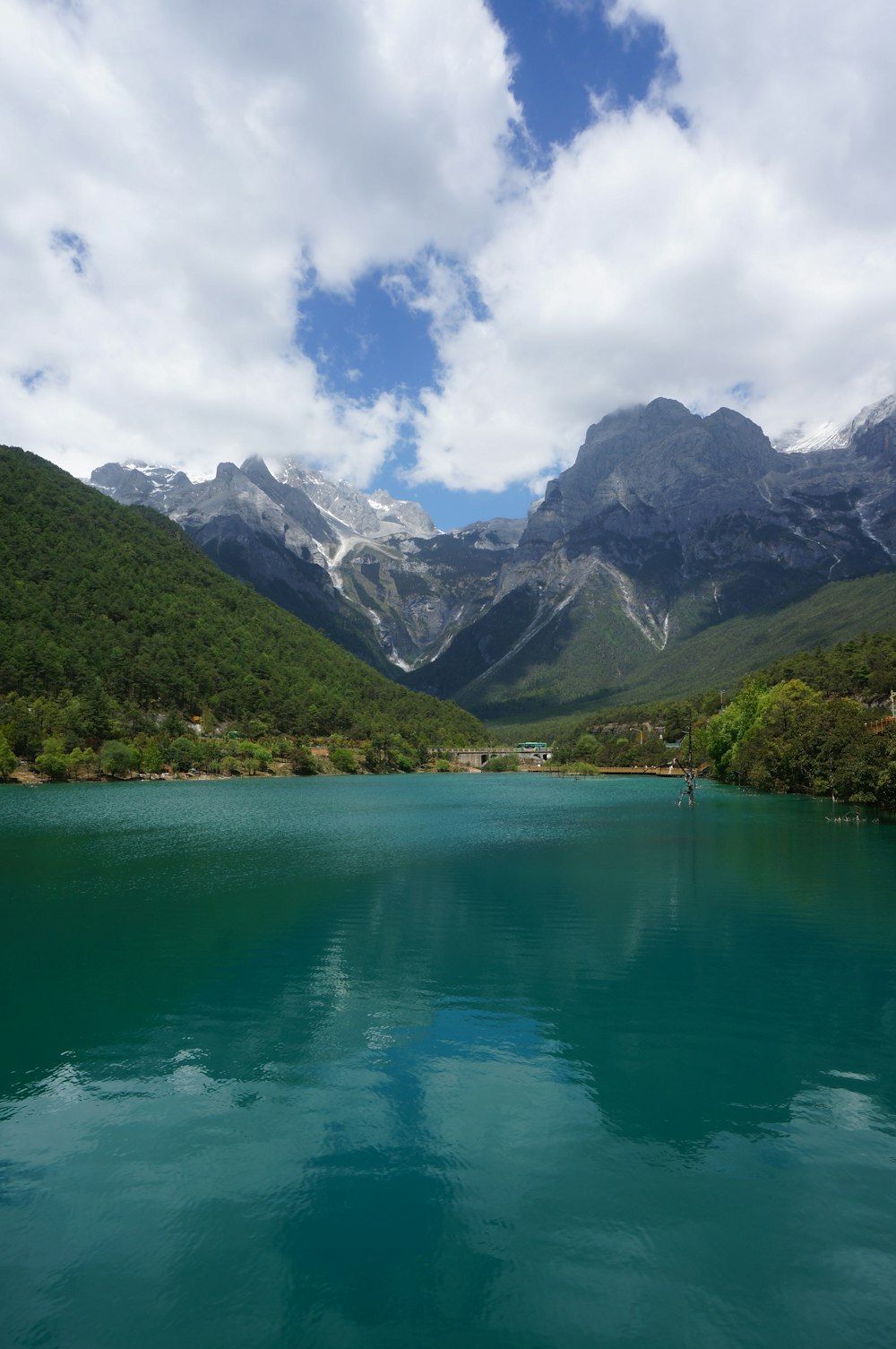 green lake surrounded by green trees and mountains under blue sky and white clouds during daytime