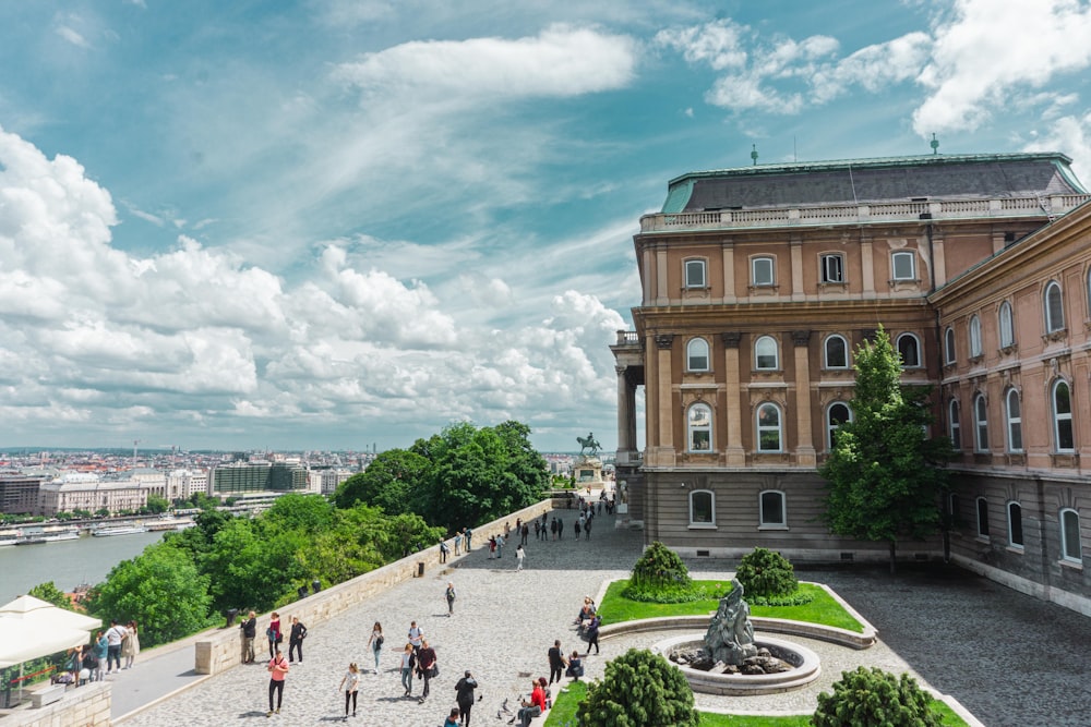 people walking on park near brown concrete building under white clouds and blue sky during daytime