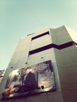 A tall building with a large advertisement for 'Dickies' featuring a man and woman on its facade. The billboard displays the brand logo and promotional text. The sky is clear with some exposed wiring attached to the structure.