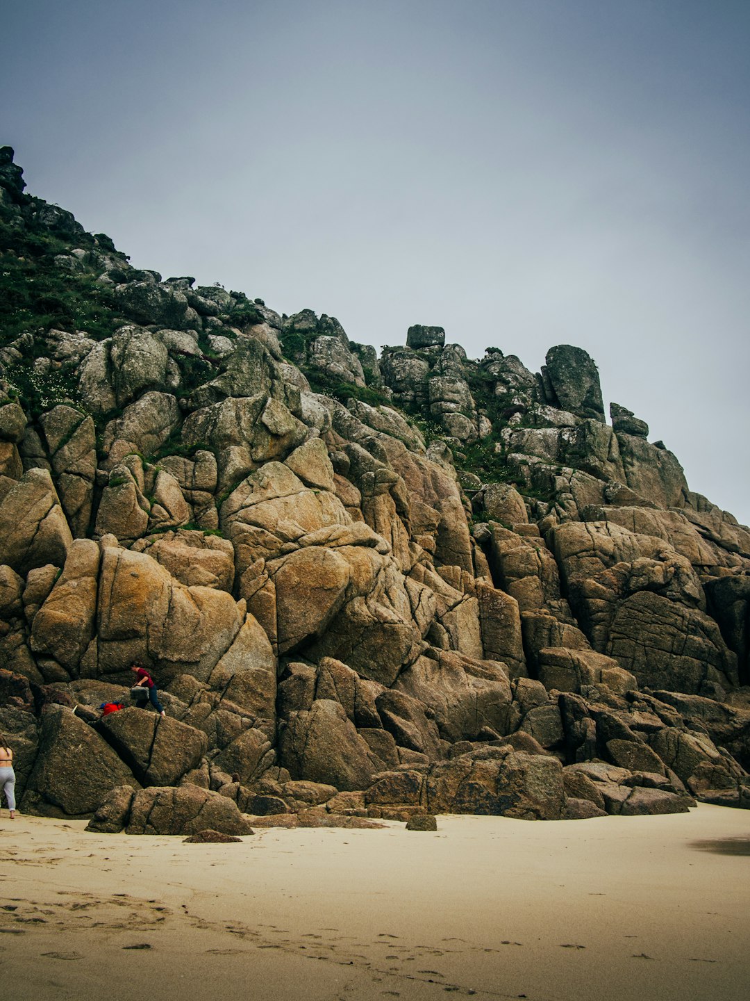 person in red shirt and black pants standing on brown rock formation during daytime