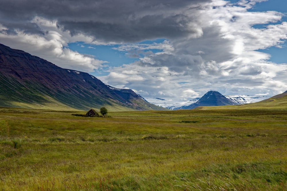 green grass field near mountain under white clouds during daytime