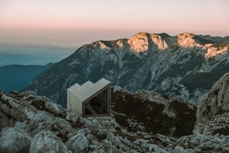 A sleek, steel-framed modular cottage nestled on a snowy mountain slope under a warm sunset.