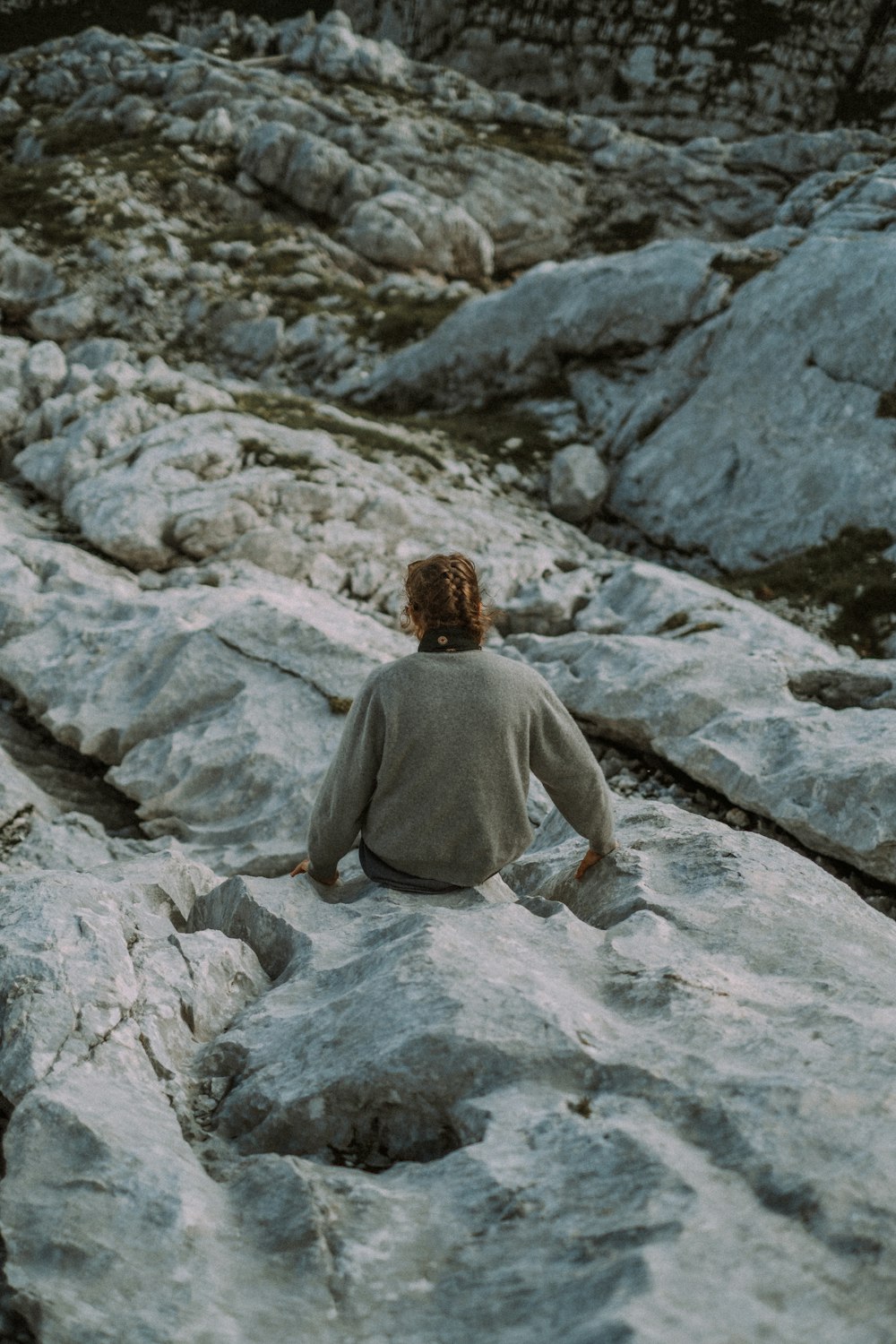 man in gray hoodie sitting on gray rock