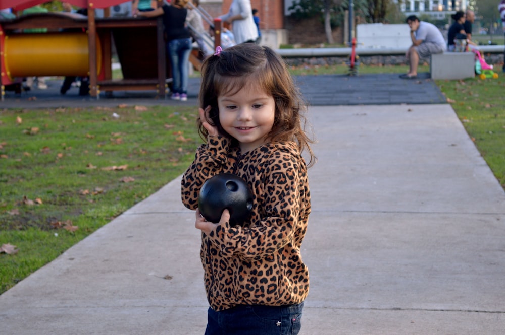 Chica con camisa de manga larga con estampado de leopardo marrón y negro y pantalones azules de pie sobre gris