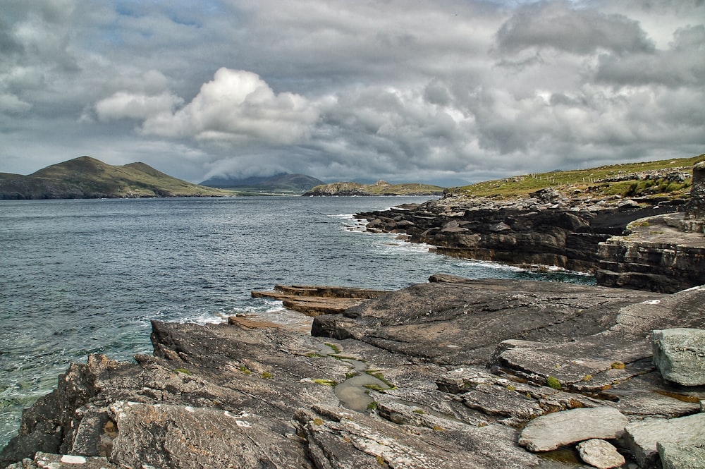 brown and green rock formation near body of water under white clouds during daytime