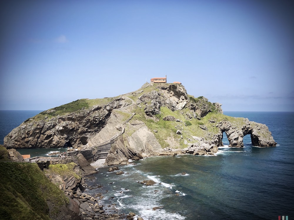 brown concrete building on green and brown mountain beside blue sea under blue sky during daytime