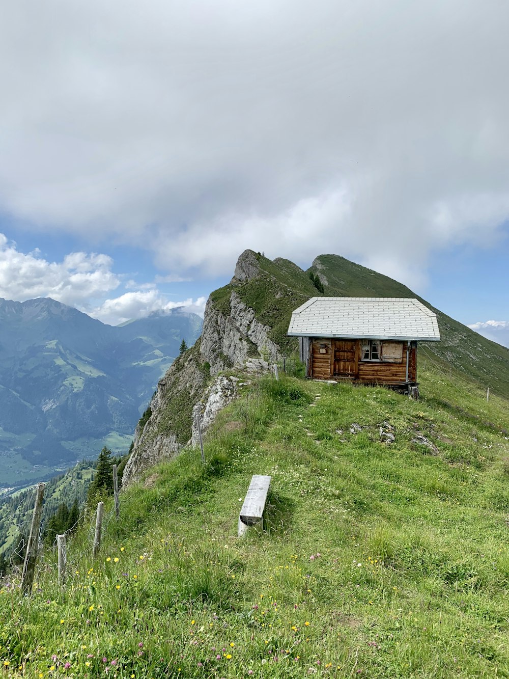 brown wooden house on green grass field near mountain under white clouds during daytime