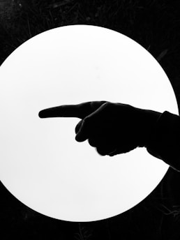 A silhouette of a hand pointing to the left against a bright circular white light background, with dark surroundings.