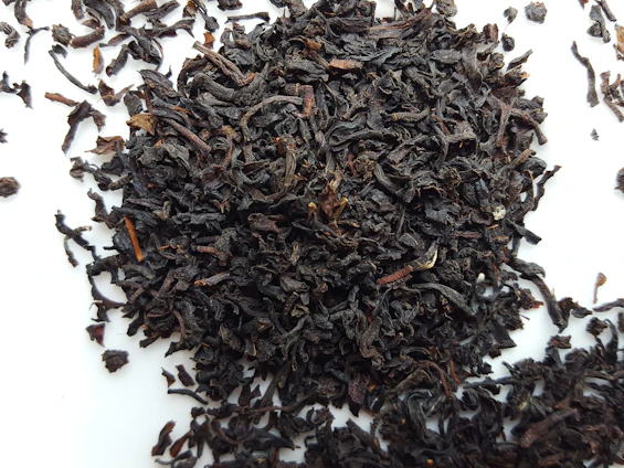 Close-up of premium loose black tea leaves spilling from a rustic sack in a wholesale warehouse setting.