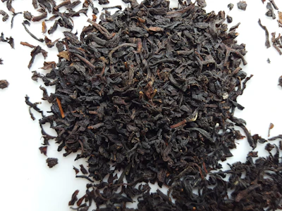 Close-up of rich black tea leaves spilling from a burlap sack onto a rustic wooden surface.