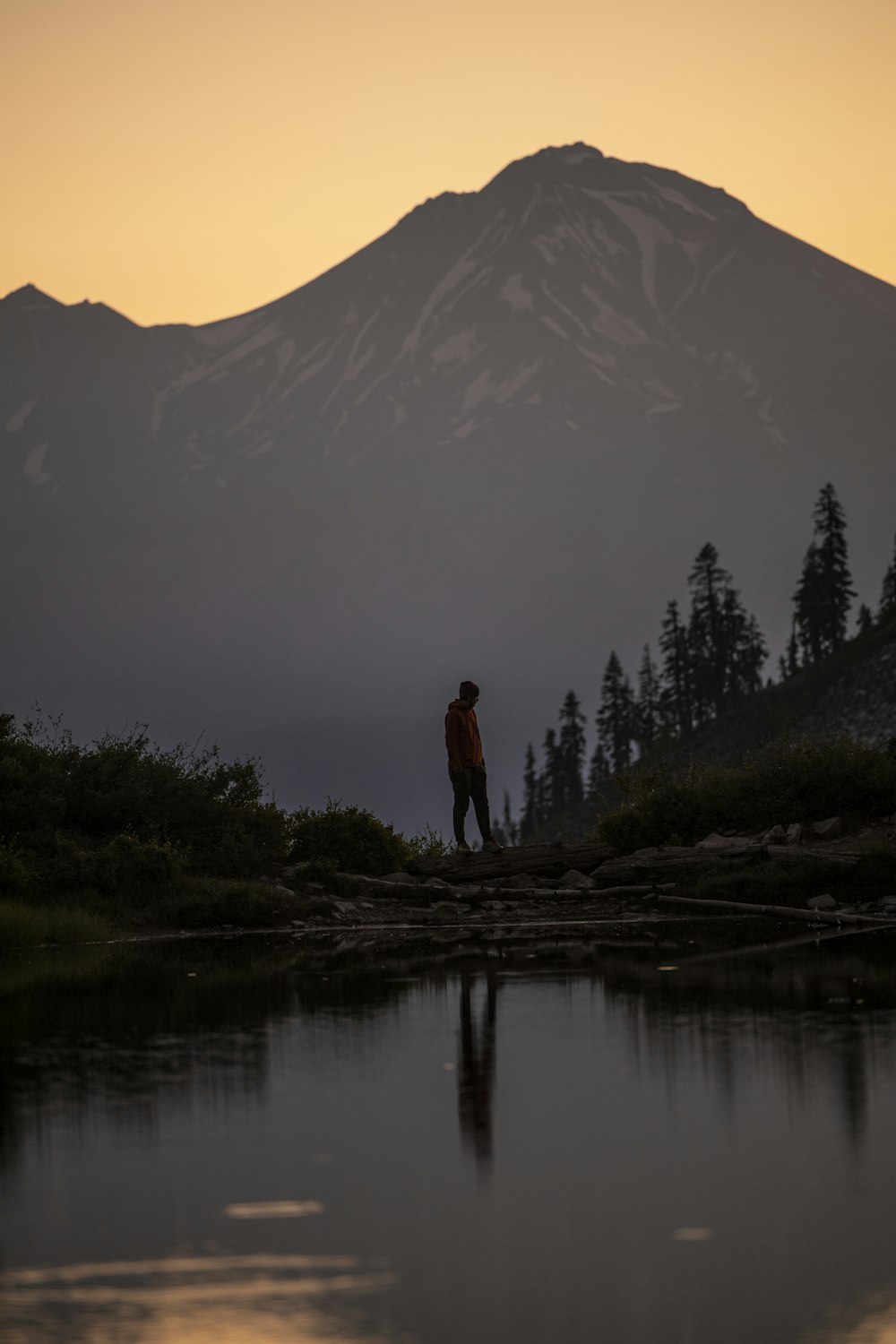 silhouette of man standing on rock near lake during daytime
