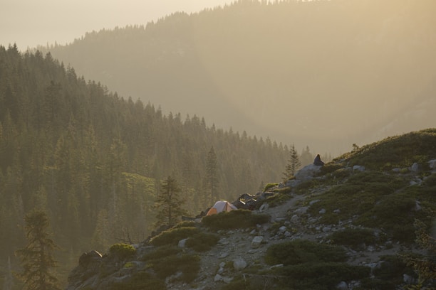 A serene mountain view at sunrise with a luxury glamping tent in the foreground.