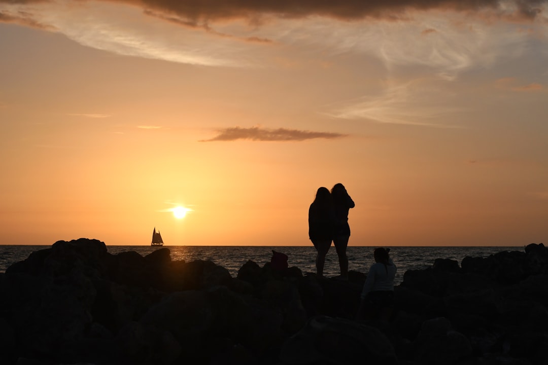 silhouette of 2 people standing on rocky shore during sunset