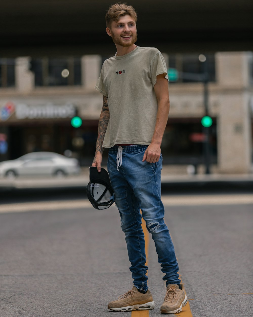uomo in t-shirt girocollo grigia e jeans blu in denim in piedi sulla strada durante il giorno