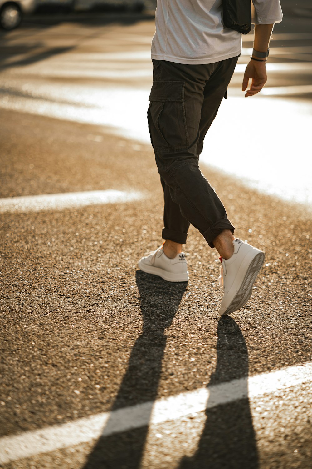 黒いズボンと白いスニーカーを履いた人が、昼間、茶色のアスファルトの道を歩いています