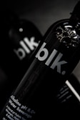 A close-up view of a black bottle with the text 'blk.' on the front. The bottle appears to contain an alkaline water beverage with a pH of 8.0 or higher. The background is dark, focusing attention on the sleek design of the bottle, with some reflections visible on its surface.