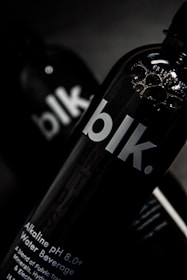 A close-up view of a black bottle with the text 'blk.' on the front. The bottle appears to contain an alkaline water beverage with a pH of 8.0 or higher. The background is dark, focusing attention on the sleek design of the bottle, with some reflections visible on its surface.