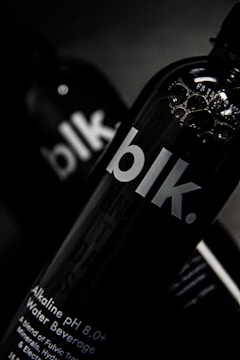 A close-up view of a black bottle with the text 'blk.' on the front. The bottle appears to contain an alkaline water beverage with a pH of 8.0 or higher. The background is dark, focusing attention on the sleek design of the bottle, with some reflections visible on its surface.