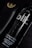 A black bottle labeled 'blk.' with text indicating it is an alkaline pH 8.0+ water beverage. The bottle is partially overlapping a black leather case with golden writing and an emblem at the corner. The setting is predominantly dark, with highlights reflecting off the glossy surfaces.