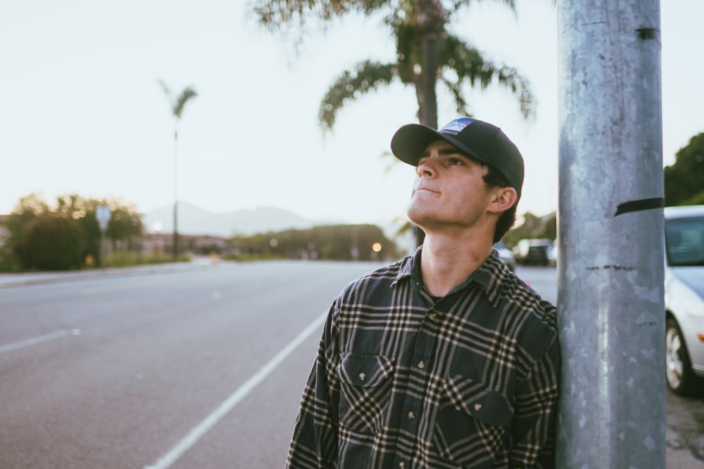 man in black and white checkered dress shirt wearing blue cap standing on gray asphalt road