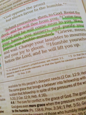 A close-up of a Bible page with highlighted text in pink and green. The main verse visible is 'Submit yourselves, then, to God. Resist the devil, and he will flee from you.' The text is written in a serif font, and there are footnotes and references included at the bottom of the page. The highlighted sections emphasize phrases about devotion and coming near to God.
