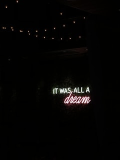 A neon sign with the message 'IT WAS ALL A dream' against a dark background, surrounded by dim fairy lights.