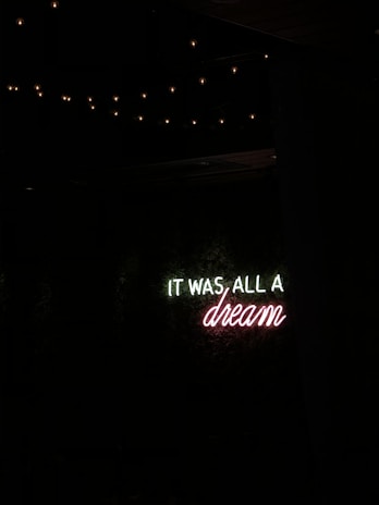 A neon sign with the message 'IT WAS ALL A dream' against a dark background, surrounded by dim fairy lights.