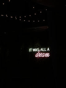 A neon sign with the message 'IT WAS ALL A dream' against a dark background, surrounded by dim fairy lights.