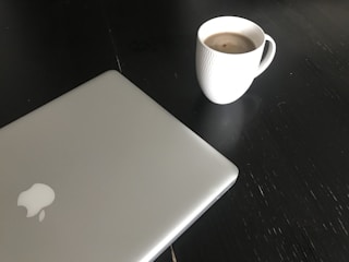 A close-up of a gently used MacBook Pro open on a cozy desk with a cup of coffee nearby.