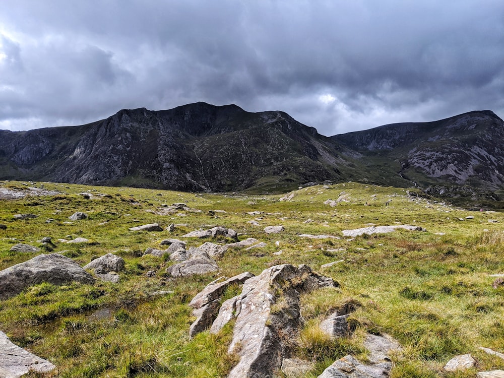 green grass field near mountain under white clouds during daytime