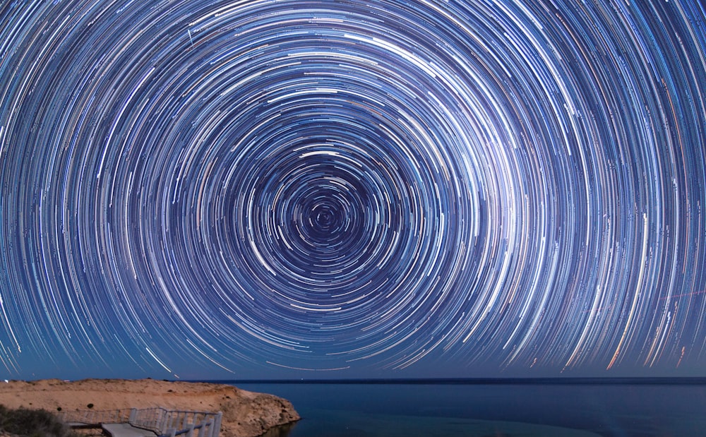 fotografia de lapso de tempo de estrelas acima do corpo de água durante a noite