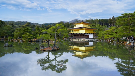 brown and green wooden house on green lake surrounded by green trees under white clouds and in Kinkaku-ji Japan