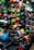 A vibrant display of various helmets in a shop, showcasing an array of colors and designs arranged neatly on shelves and hanging on walls. Both full-face and open helmets are visible, along with an assortment of patterns and styles. The shop is well-lit, with a bustling, busy feel.