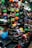 A vibrant display of various helmets in a shop, showcasing an array of colors and designs arranged neatly on shelves and hanging on walls. Both full-face and open helmets are visible, along with an assortment of patterns and styles. The shop is well-lit, with a bustling, busy feel.
