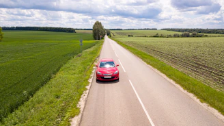 red car on road between green grass field during daytime